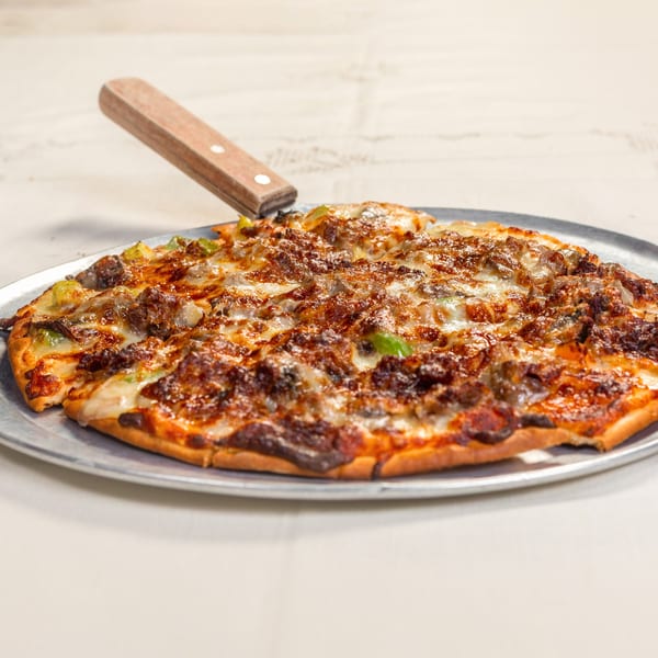 A Rookies Sports Bar & Grill pizza with meat, cheese, and green peppers on a metal pan.