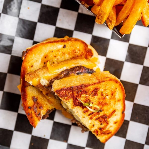 Grilled cheese burger with fries on checkered paper, a classic sports bar meal.