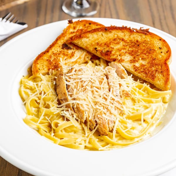 Chicken Alfredo pasta with grilled chicken, parmesan cheese, and two slices of garlic bread.