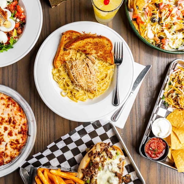 Overhead view of various sports bar dishes, including pasta, nachos, pizza, and a cheesesteak.
