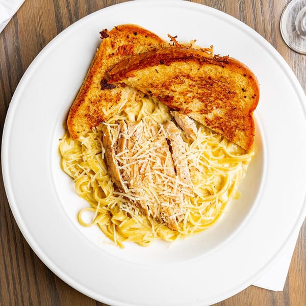 Overhead view of chicken alfredo pasta with two slices of garlic bread on a white plate.