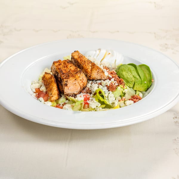 Salmon salad with avocado, blue cheese, bacon bits, and tomatoes on a white plate.